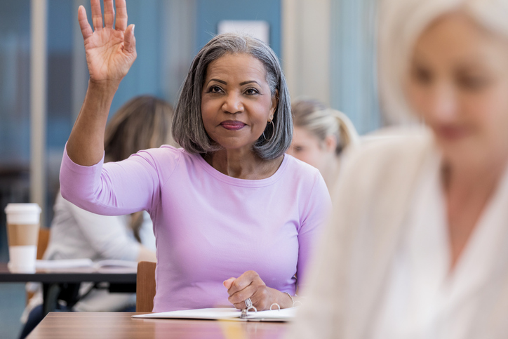 Attractive mature African American woman raises hand in class