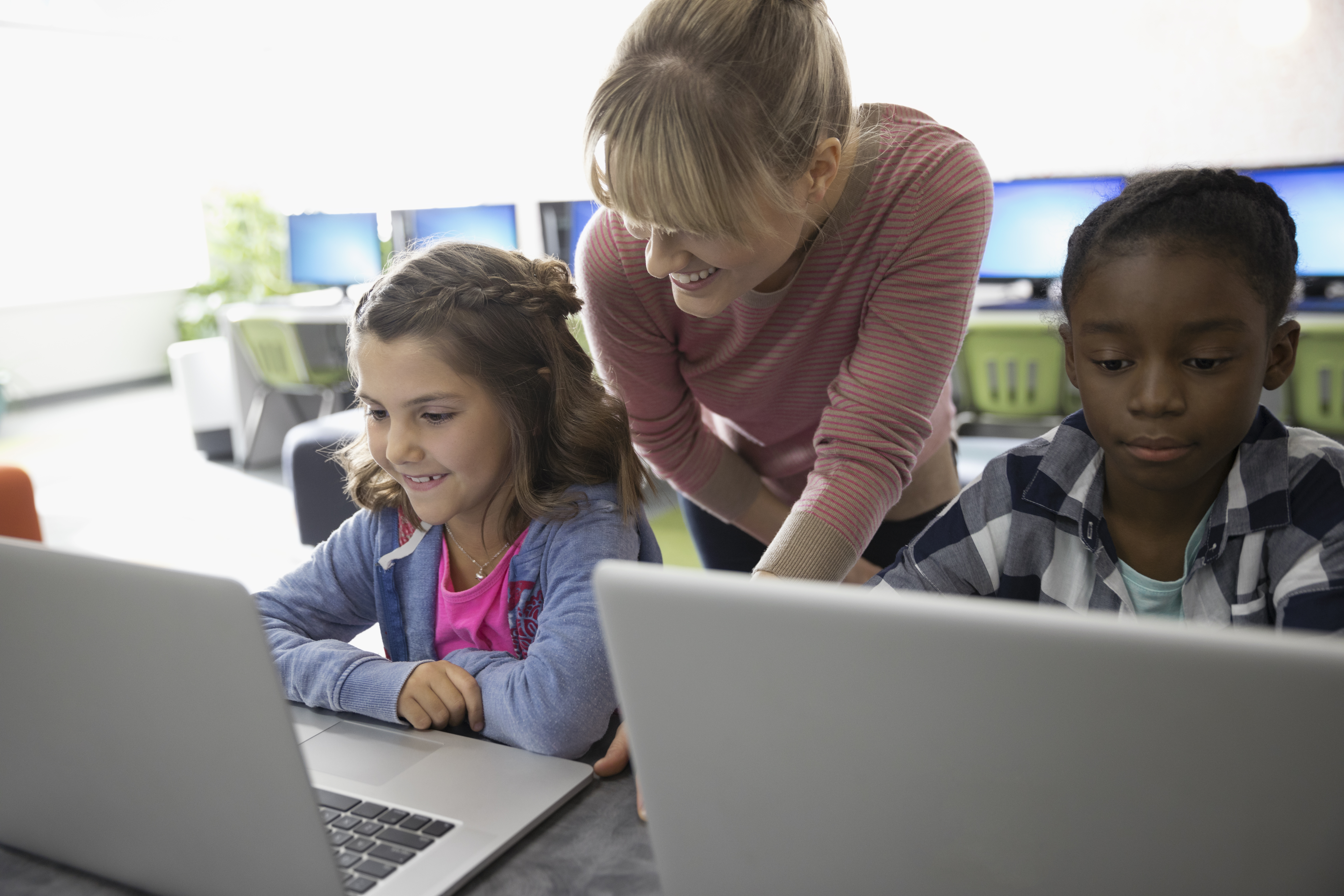 Female teacher and pre-adolescent girls using laptops in classroom