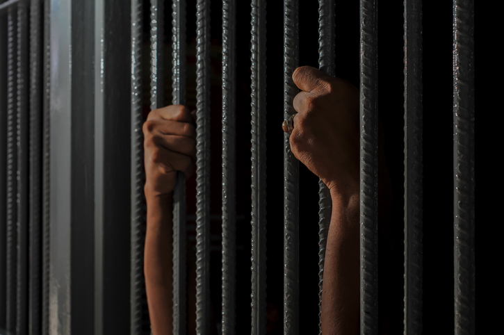 prisoner's hands behind bars with black background