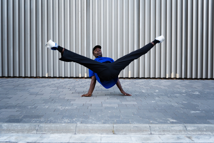 Urban breakdancer performing dynamic freeze pose, spreading legs wide against city background, highlighting street dance power and skill