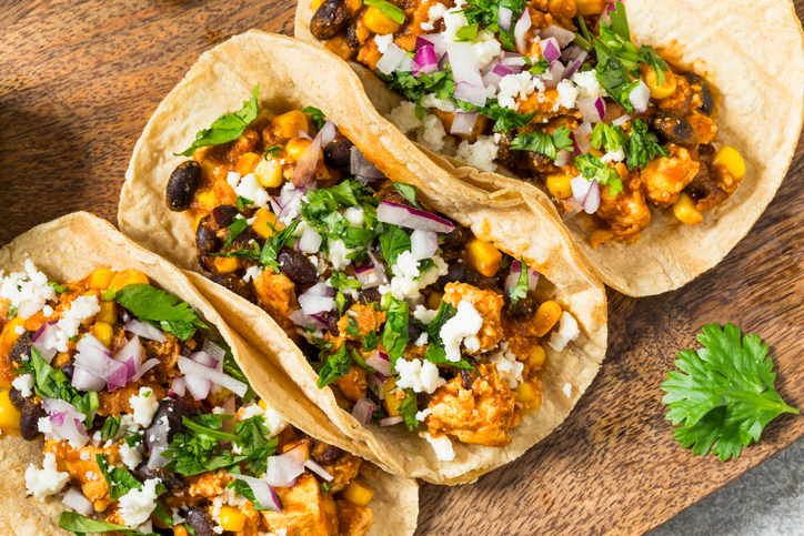 Delicious homemade chicken and black bean street tacos with corn, red onion, cilantro, and cotija cheese on a wooden cutting board, viewed from directly above